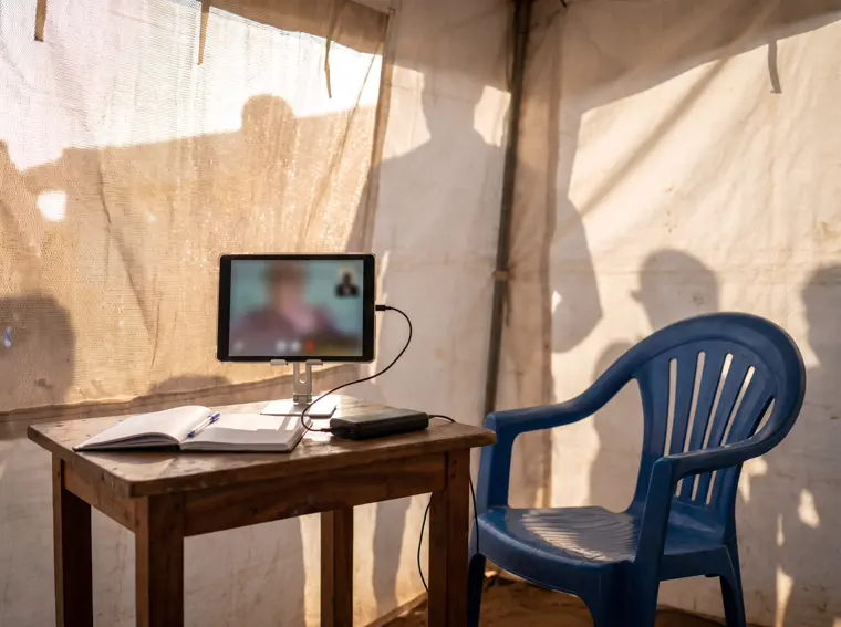 Interior de uma tenda de consulta numa feira de saúde: tablet num suporte com a chamada de vídeo, cadeira e bateria de reserva